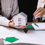 Équipe d'agence immobilière présentant maquette de maison et documents contractuels lors d'une transaction