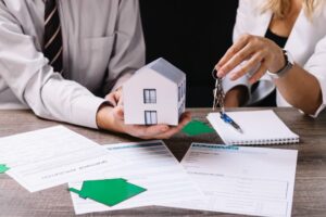 Équipe d'agence immobilière présentant maquette de maison et documents contractuels lors d'une transaction
